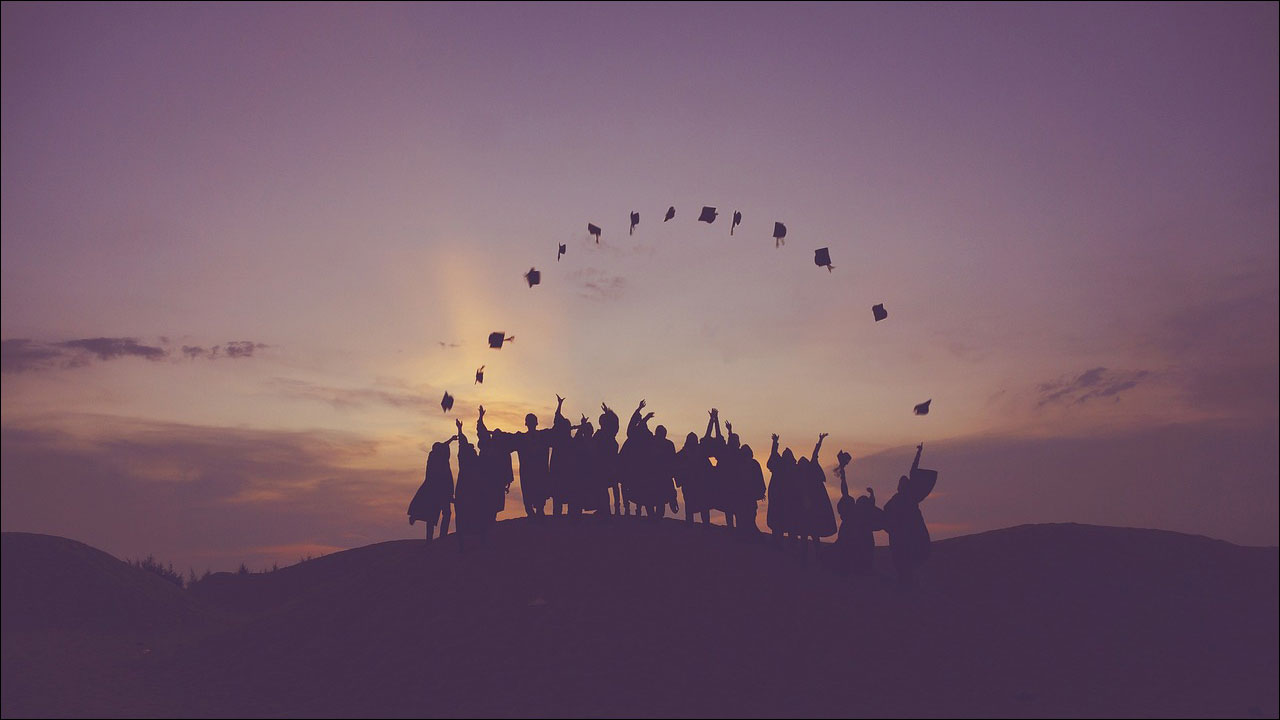Silhouettes of graduate students with linked hands on top of a hill 